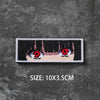 A black and white embroidered badge featuring a stylized eye design on a gray textured background.