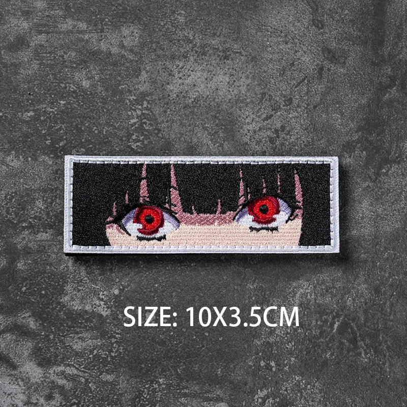 A black and white embroidered badge featuring a stylized eye design on a gray textured background.