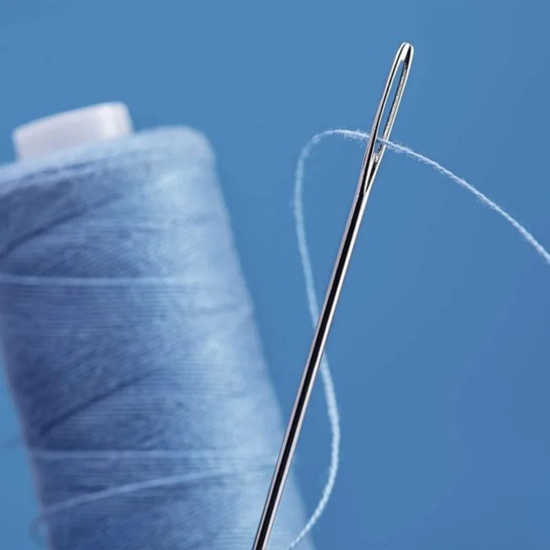 A pair of large eye hand sewing needles with a white thread are shown next to a blue spool of thread.