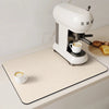 A white electric coffee grinder sits on a beige mat next to a white cup and some bread.