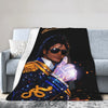 A dark graphic print featuring a person in a blue suit with gold accents and sparkling light effects on a soft throw blanket.