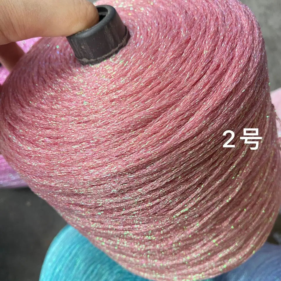 A close-up of a skein of pink glitter metallic yarn being held by a hand.