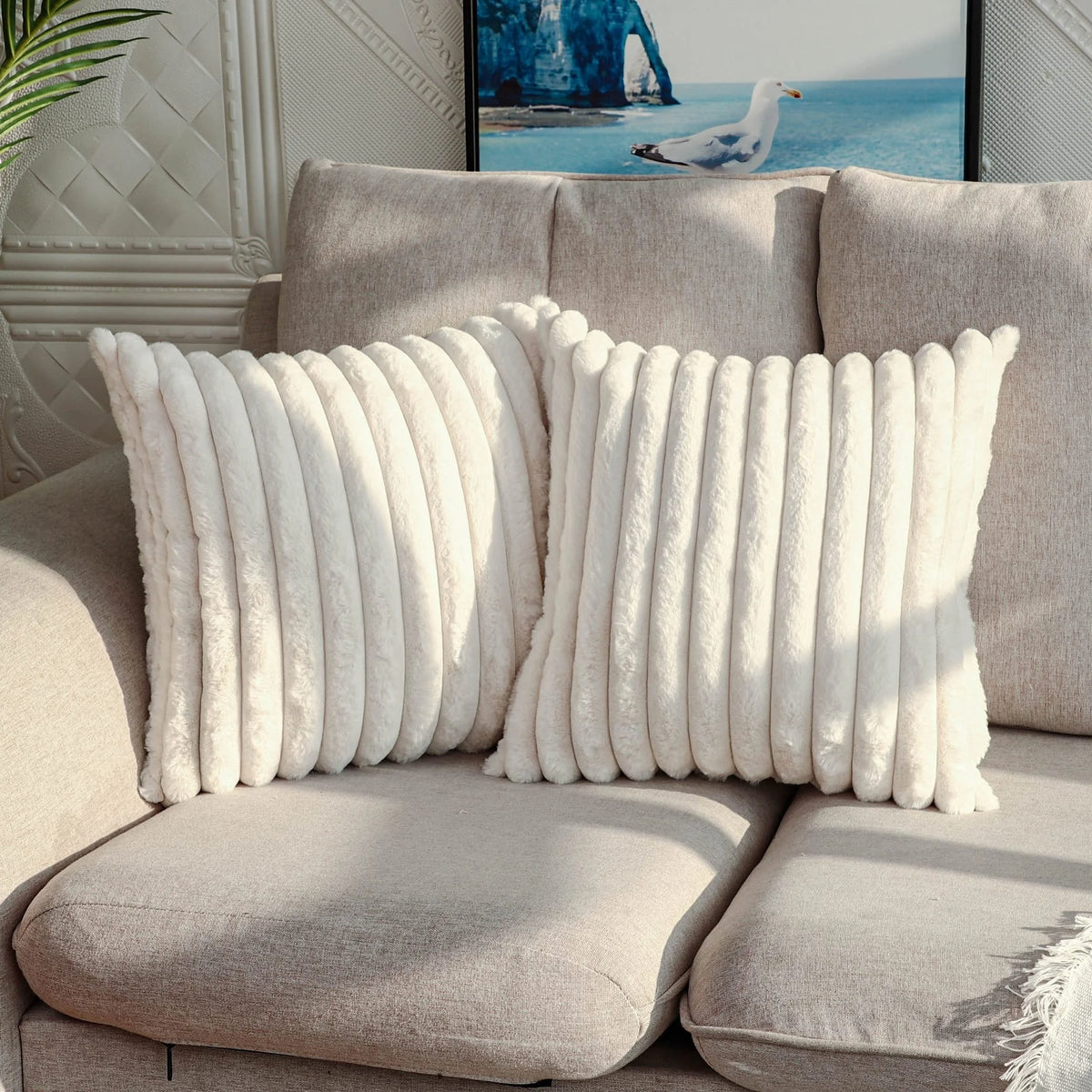 A pair of fluffy white stripe corduroy pillow covers resting on a light beige sofa.