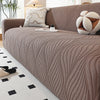 A beige stretch sofa cover featuring a vertical ribbed texture and an elastic edge, displayed in a living room setting.
