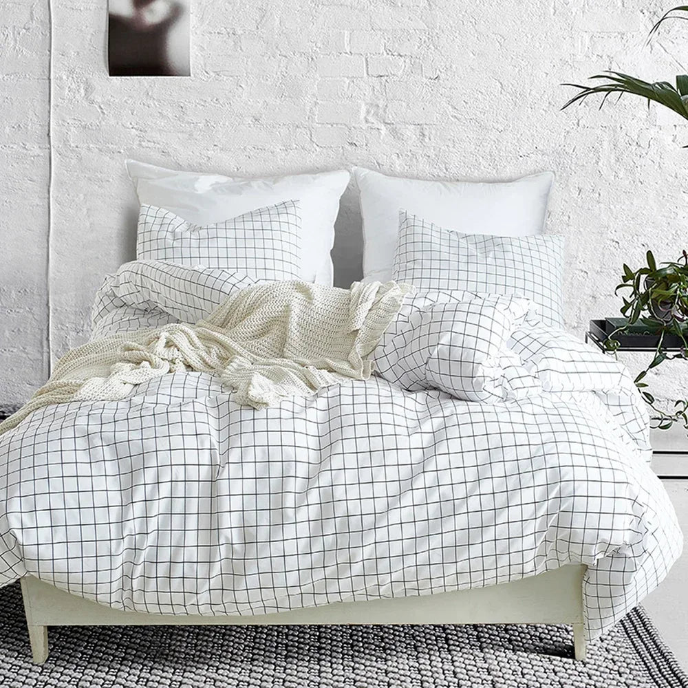 A white and gray plaid duvet cover set with cream throw pillows on a bed against a white brick wall.