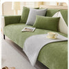 A green sofa protection cover with gray cushions and a light-colored blanket on a white sofa.