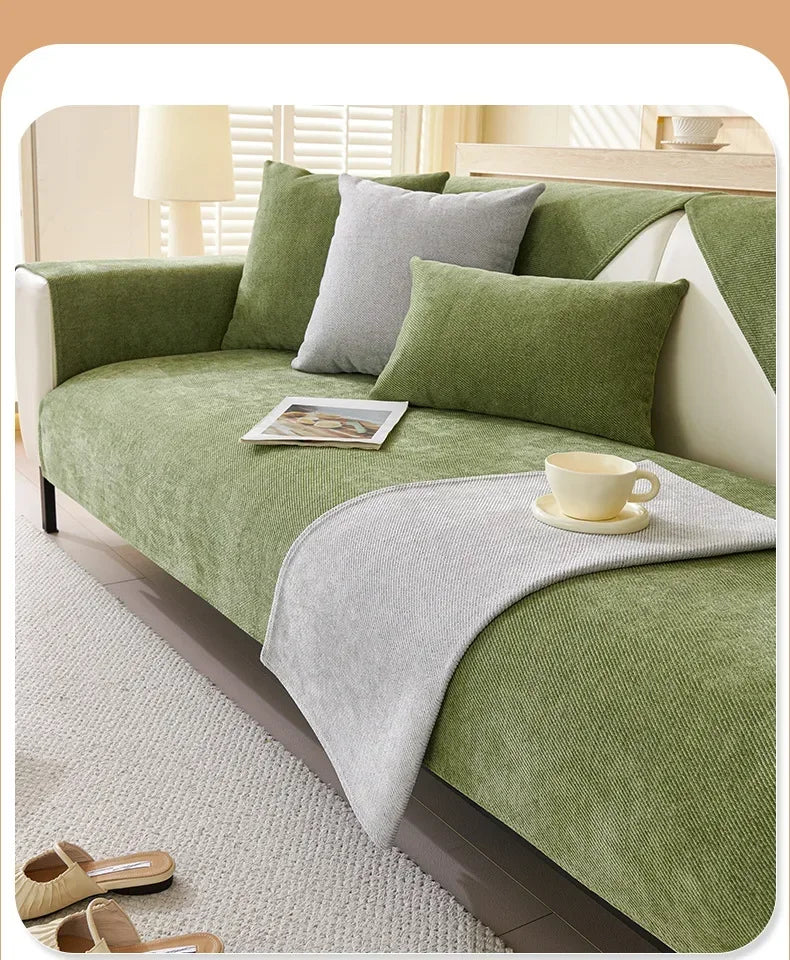 A green sofa protection cover with gray cushions and a light-colored blanket on a white sofa.