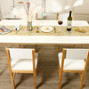 A white wooden dining table set with a woven runner, wine glass, and floral centerpiece.