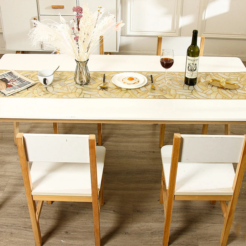 A white wooden dining table set with a woven runner, wine glass, and floral centerpiece.