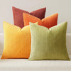 A set of four textured throw pillows in shades of orange, terracotta, and lime green.