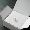 A white embroidery bobbin thread is placed inside a cardboard box.