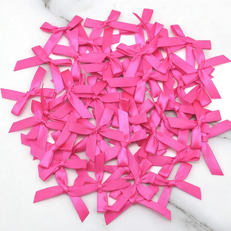 A pile of bright pink satin ribbon bows for crafts and decor scattered on a white marble surface.