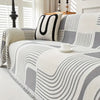 A close-up of a plush sofa cover featuring a modern geometric pattern in shades of gray and white with a black accent pillow.