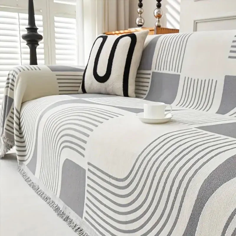 A close-up of a plush sofa cover featuring a modern geometric pattern in shades of gray and white with a black accent pillow.