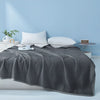 A dark gray quilted blanket is displayed on a bed against a light blue wall with white pillows and a small plant.