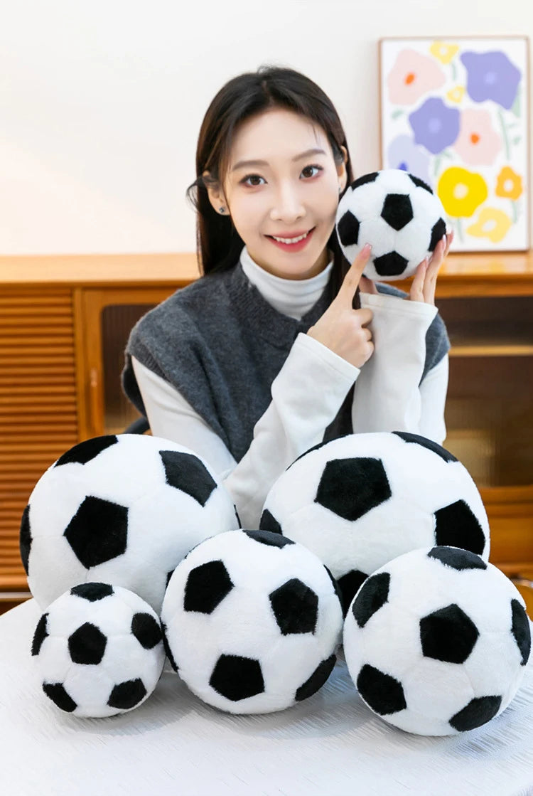 A woman holds a black and white football plush toy against a light background.