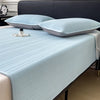 Light blue striped cooling ice silk bed pad placed on a bed with a dark headboard.