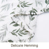 Close-up of a white muslin swaddle blanket with green leaf print, showing delicate hemming.