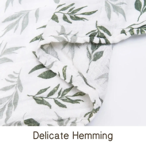 Close-up of a white muslin swaddle blanket with green leaf print, showing delicate hemming.