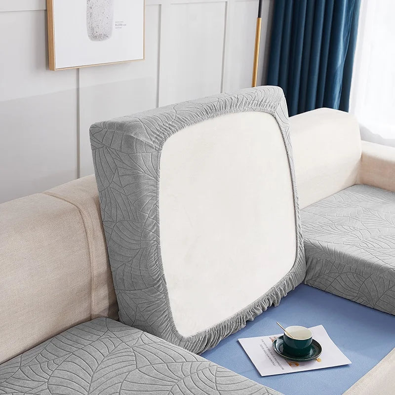 A close-up of a light gray waterproof jacquard stretch sofa cover with a white cushion on a beige sofa.