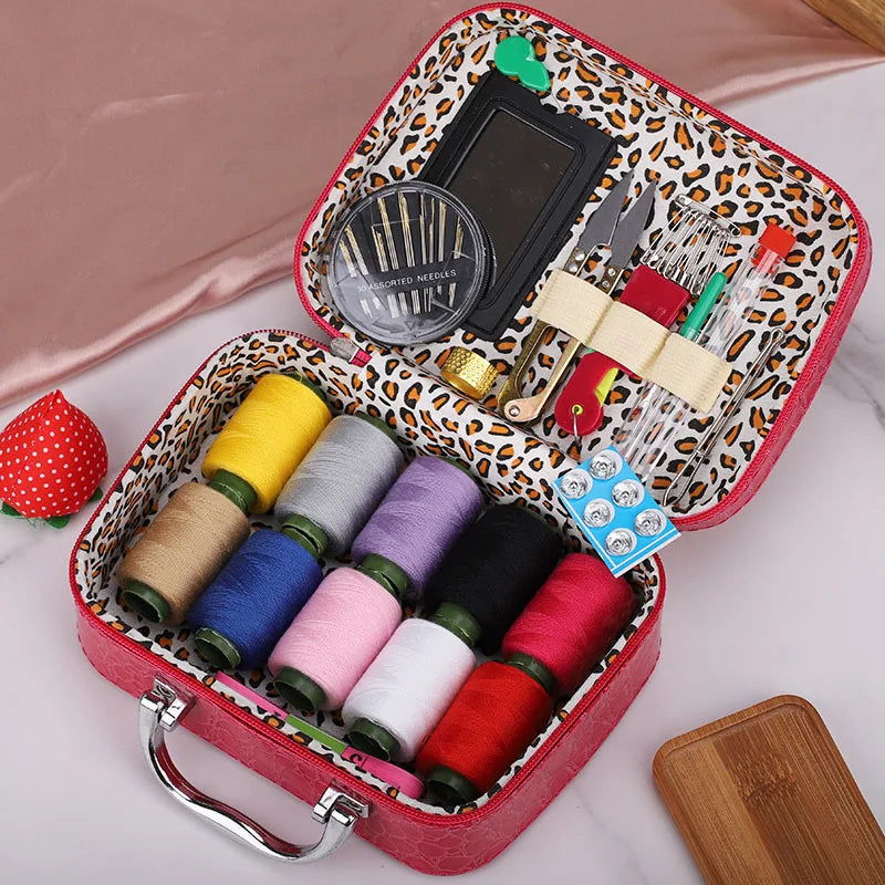 A red leather sewing kit box containing various colored threads, needles, and tools on a pink background.