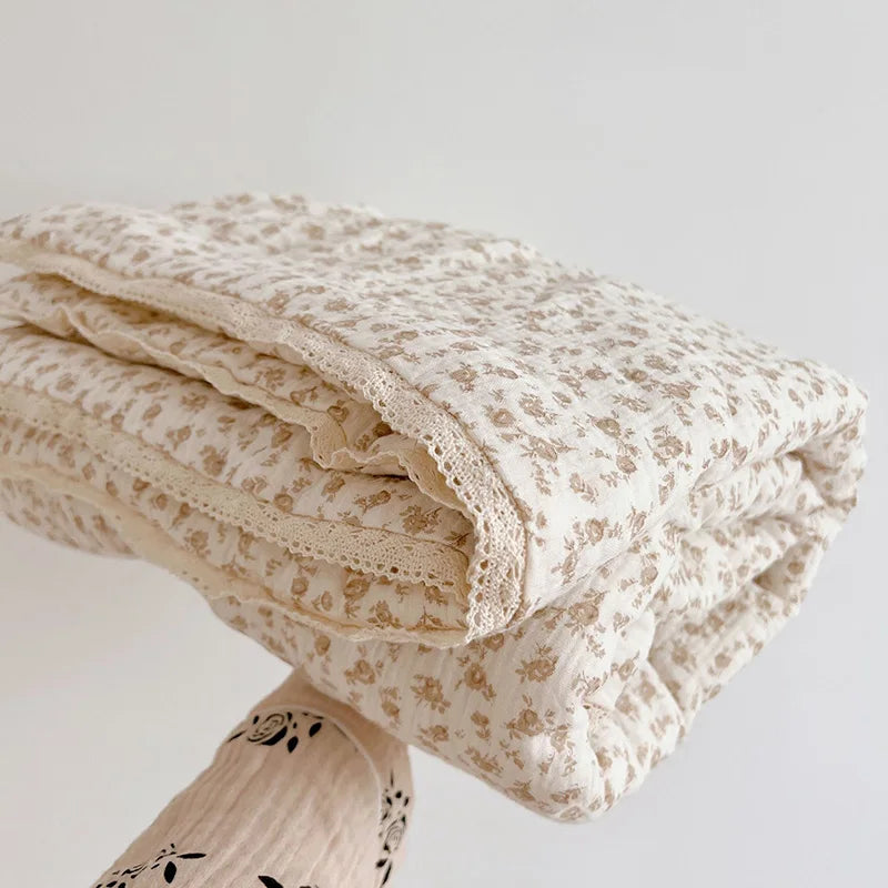 A rolled floral print muslin blanket in cream and beige tones