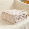 A folded light pink checkered fleece throw blanket resting on a white, fluffy surface.