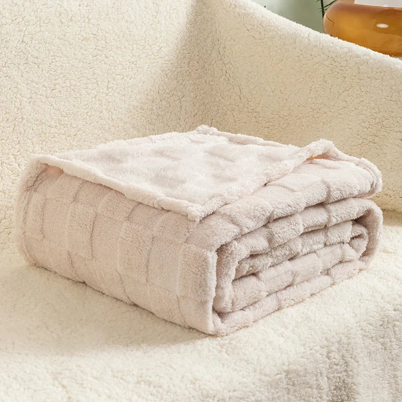 A folded light pink checkered fleece throw blanket resting on a white, fluffy surface.