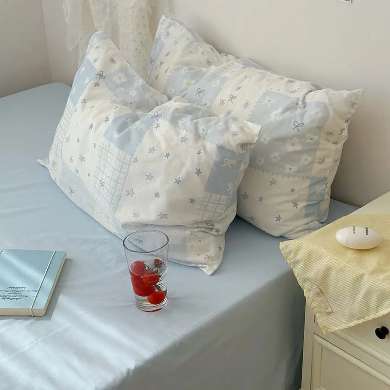 A set of three light blue floral duvet covers and pillowcases with white accents displayed on a bed.