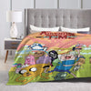 A colorful cartoon-themed throw blanket featuring characters and text, displayed on a bed with a gray upholstered headboard.