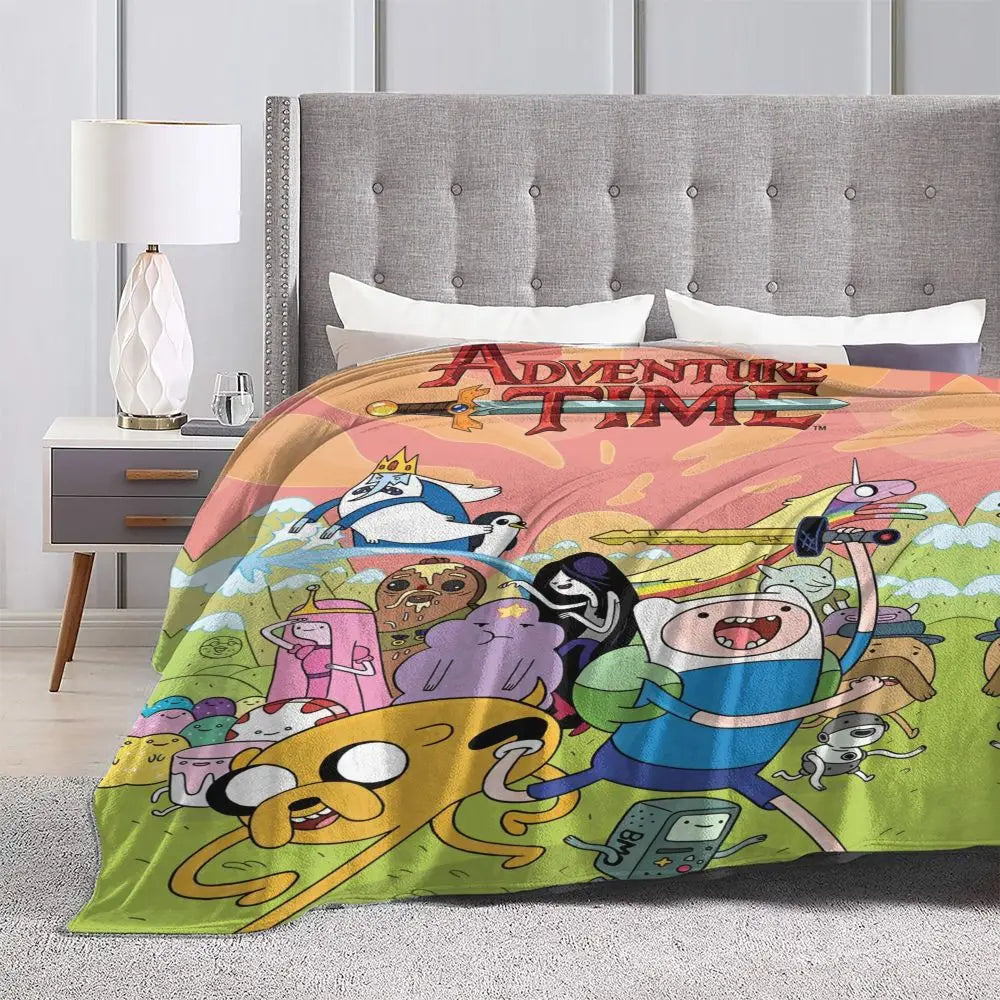 A colorful cartoon-themed throw blanket featuring characters and text, displayed on a bed with a gray upholstered headboard.