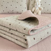 A stack of pink and green quilted fabric textiles with a subtle pattern resting on a pink surface.