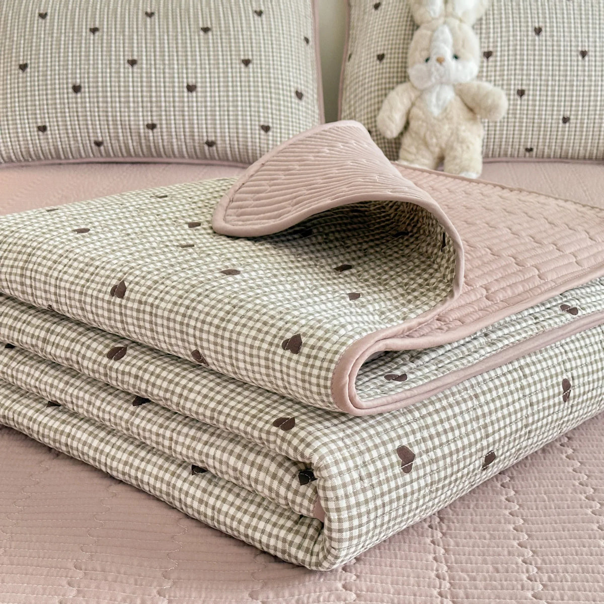 A stack of pink and green quilted fabric textiles with a subtle pattern resting on a pink surface.