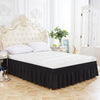 A white bed with a black ruffled skirt and a cream upholstered headboard in a bright room.