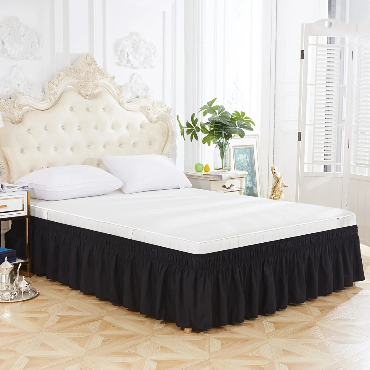 A white bed with a black ruffled skirt and a cream upholstered headboard in a bright room.