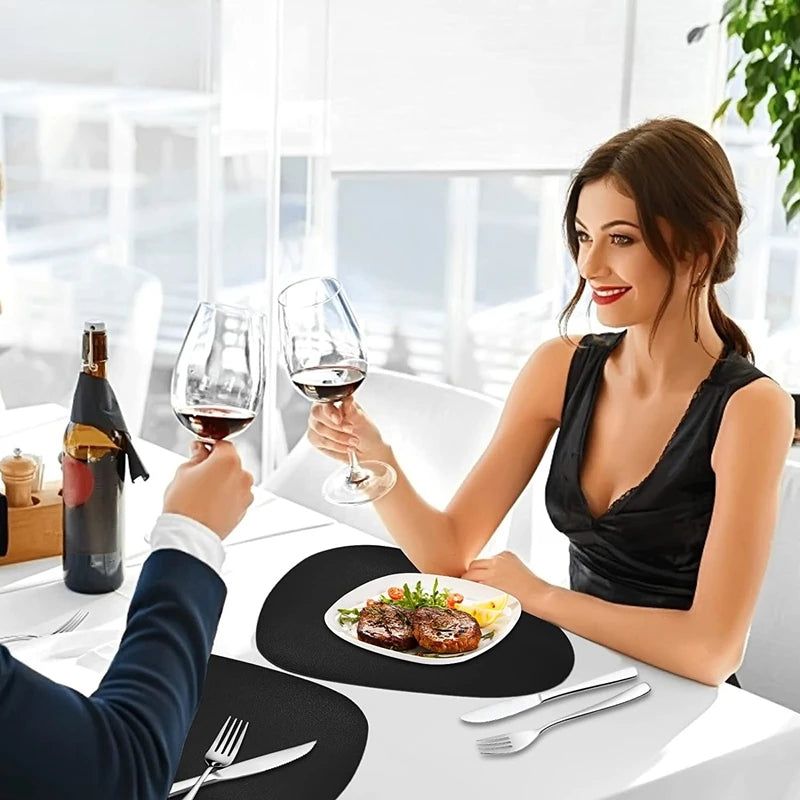 A woman is dining at a table with wine glasses and food, set on black vinyl placemats.