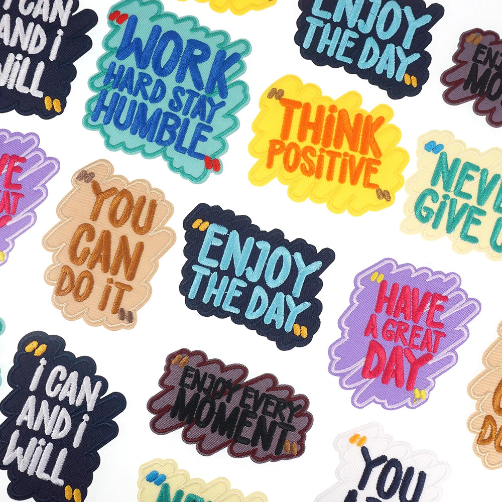 A collection of iron-on embroidered text patches with positive phrases like Work Hard Stay Humble and Enjoy The Day.
