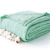 A teal knitted gauze blanket rolled up next to a cluster of white cotton bolls.