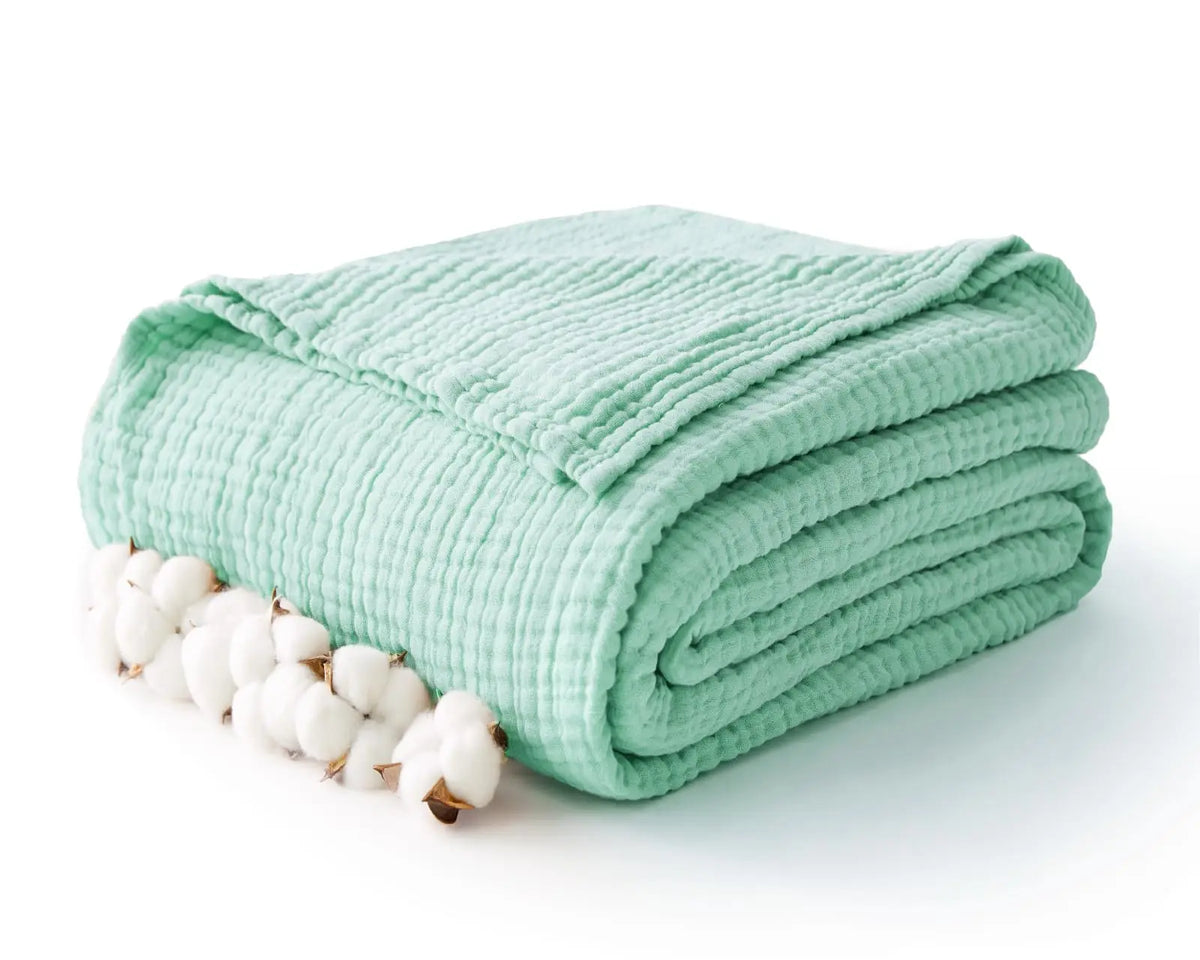 A teal knitted gauze blanket rolled up next to a cluster of white cotton bolls.