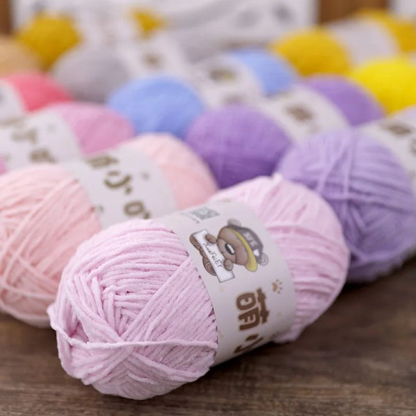 A pile of pink chenille yarn balls in various shades are displayed on a wooden surface.