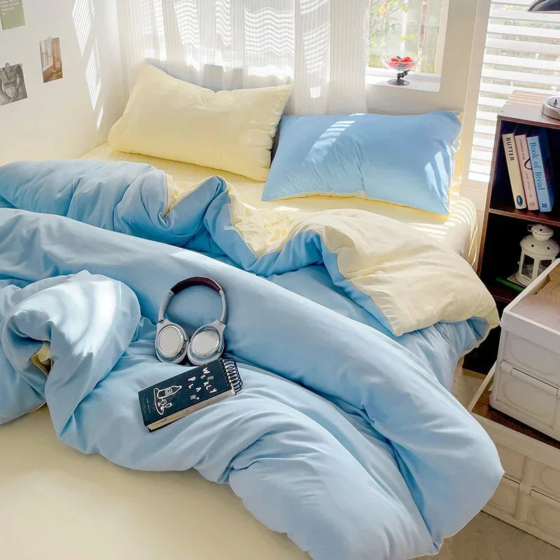 A light blue cotton bed linen set with yellow accents is displayed on a bed with white blinds.