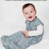 A baby wearing a light blue sleeveless sleep sack for sleeping on a white bed.