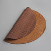 A curved piece of hand-woven bamboo tea mat in a warm brown color.
