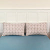A set of two plaid pillow covers in beige and brown tones displayed against a white wainscoting wall.