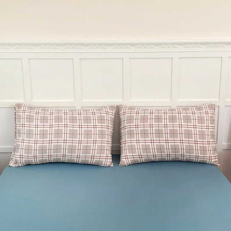 A set of two plaid pillow covers in beige and brown tones displayed against a white wainscoting wall.