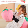 A woman is holding a pink plush strawberry throw pillow in a bright indoor setting.