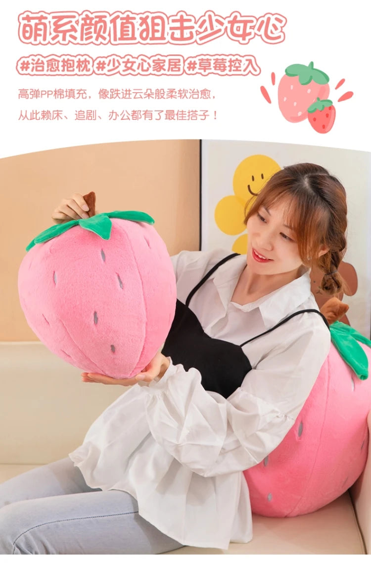 A woman is holding a pink plush strawberry throw pillow in a bright indoor setting.