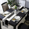 A modern geometric placemat set featuring black and white patterns with gold cutlery and green plant accents on a dining tabl