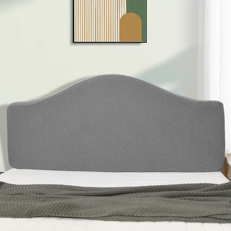 A gray soft elastic headboard cover is shown on a bed, with a light green wall and framed artwork in the background.