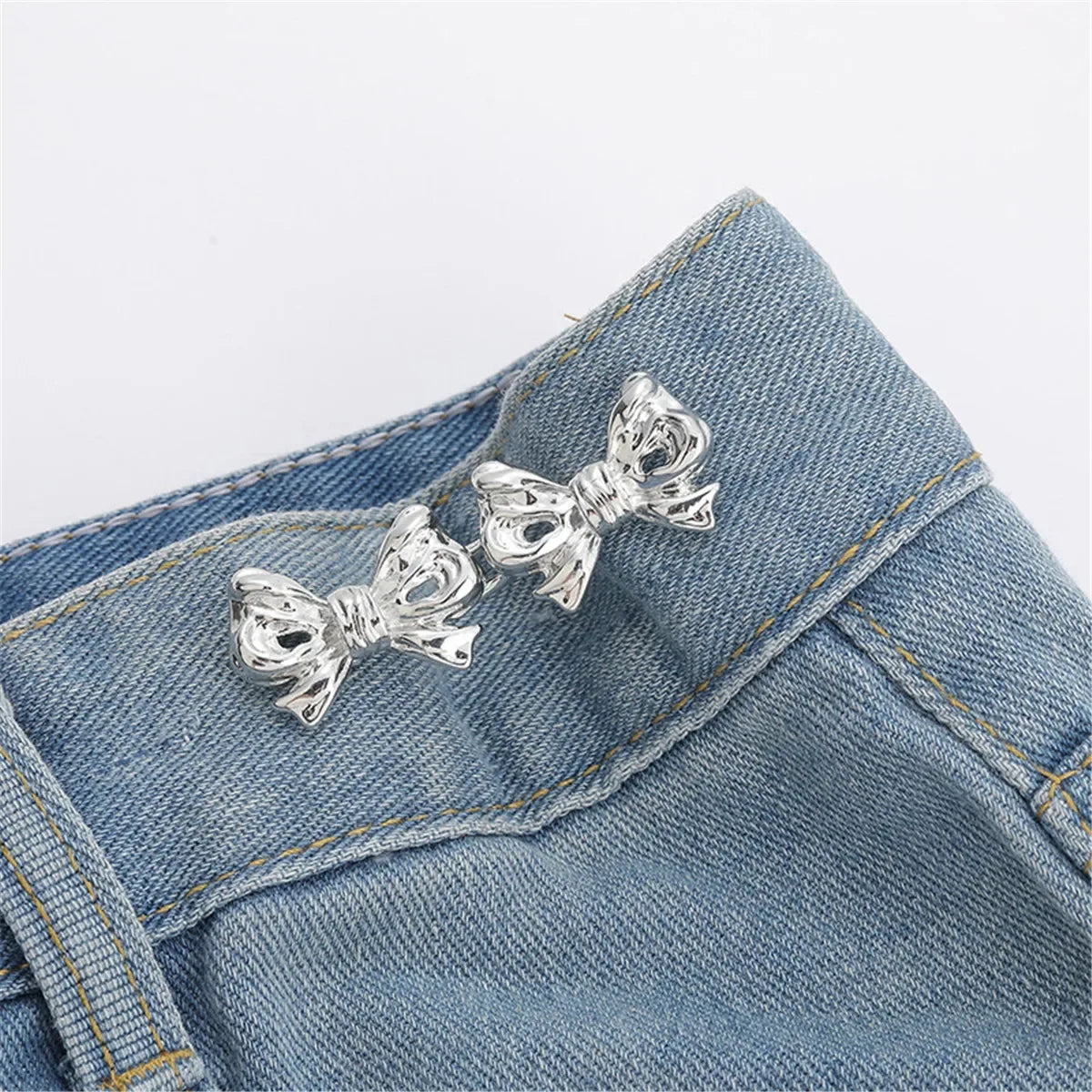 Silver bow-shaped button clips attached to a denim jean fabric
